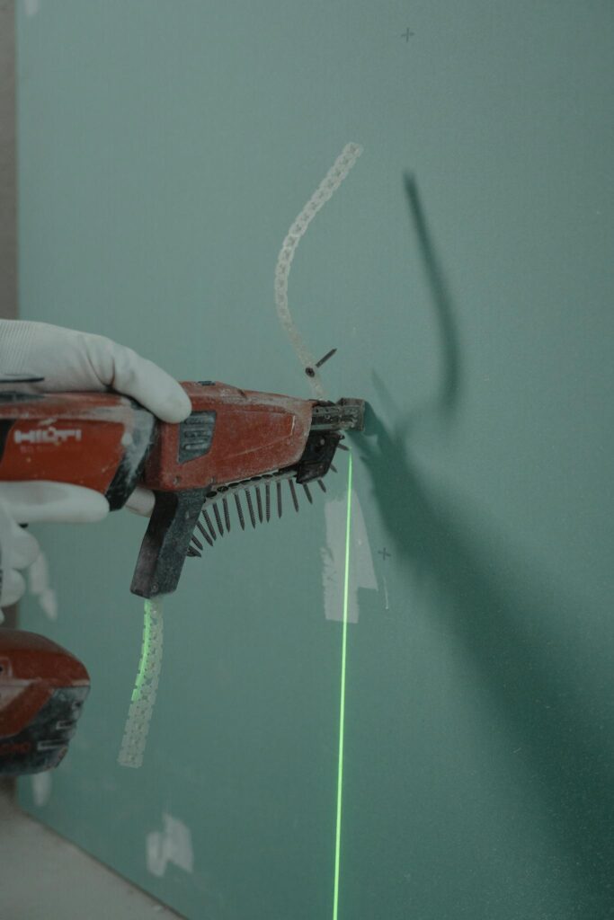 Close-up of a handyman using a laser level and nail gun for drywall installation.