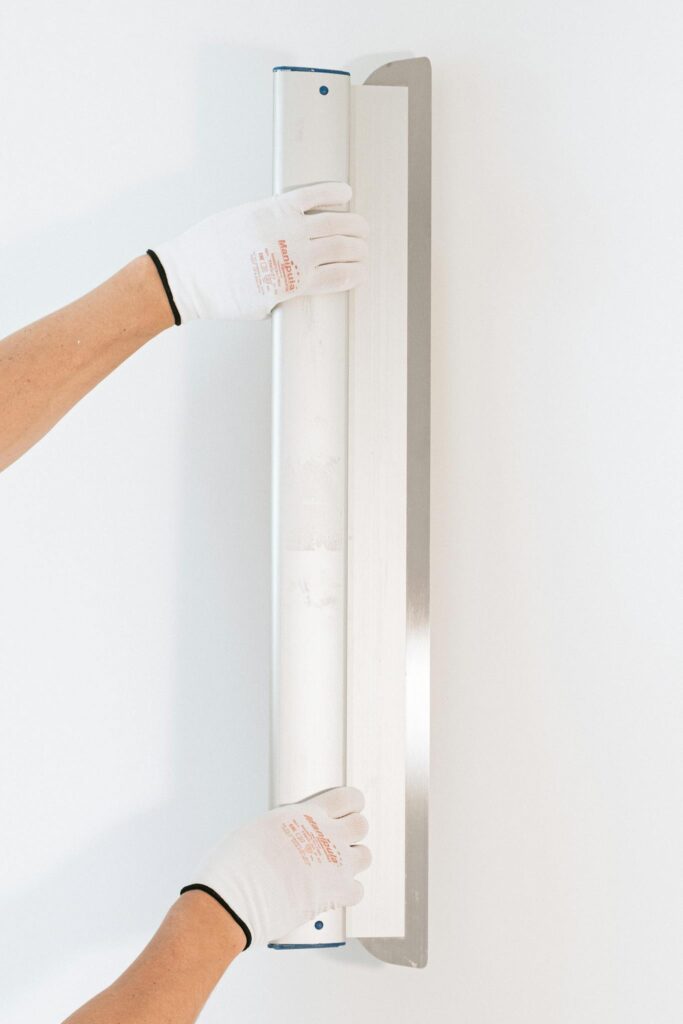 Hands of a worker smoothing a wall with a tool, wearing gloves, close-up on white background.